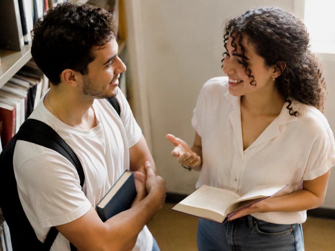 Conversa em pé entre as estantes da escola, com folhas de anotação na mão de quem discute